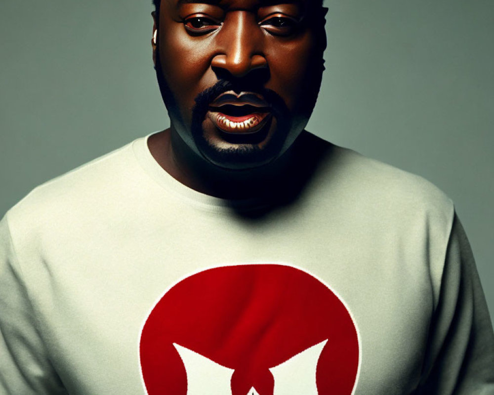 Bearded man in grey sweatshirt with red and white logo on grey background