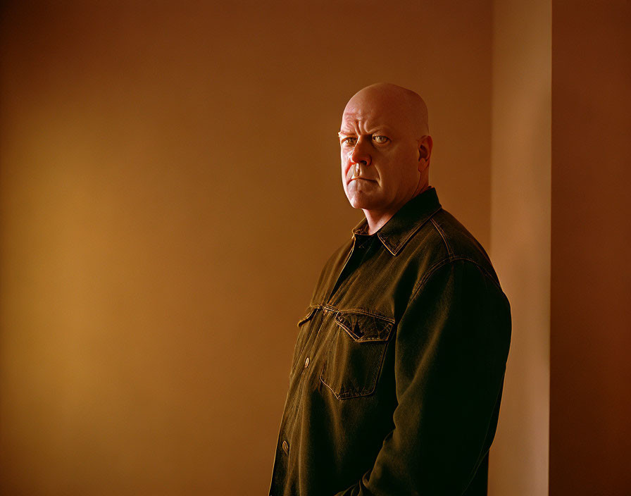 Stern bald man in dark shirt against orange-brown background