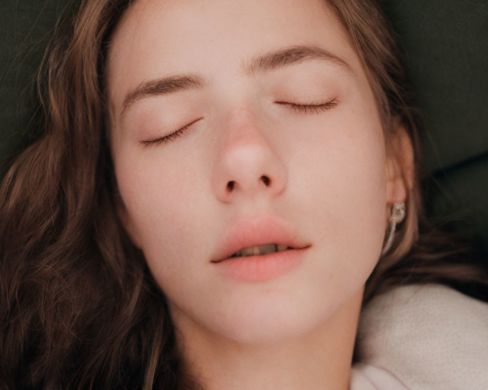 Serene woman with closed eyes on green cushion with soft brown hair