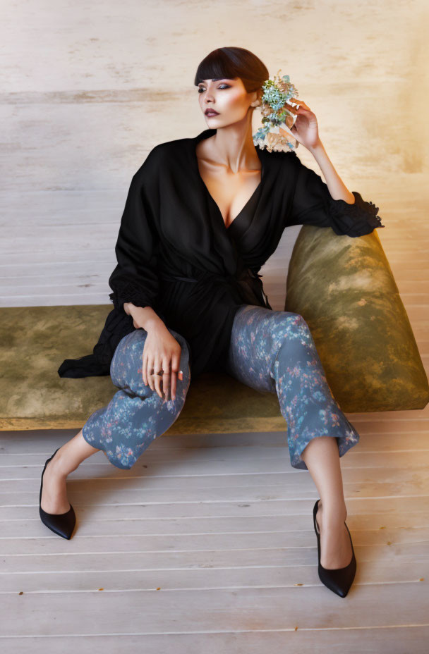 Elegant woman in black robe with flower on plush bench, warm wooden backdrop