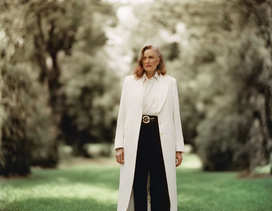 Professional individual in white jacket and black pants against blurred green background.