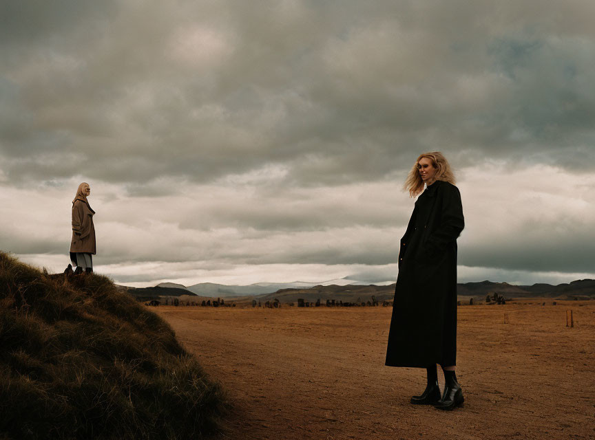 Two women on desolate road under stormy skies, gazing into distance