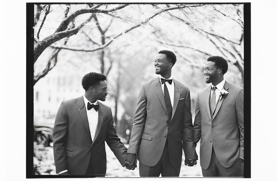 Three Men in Suits and Bow Ties Celebrate Under Bare Tree Canopy