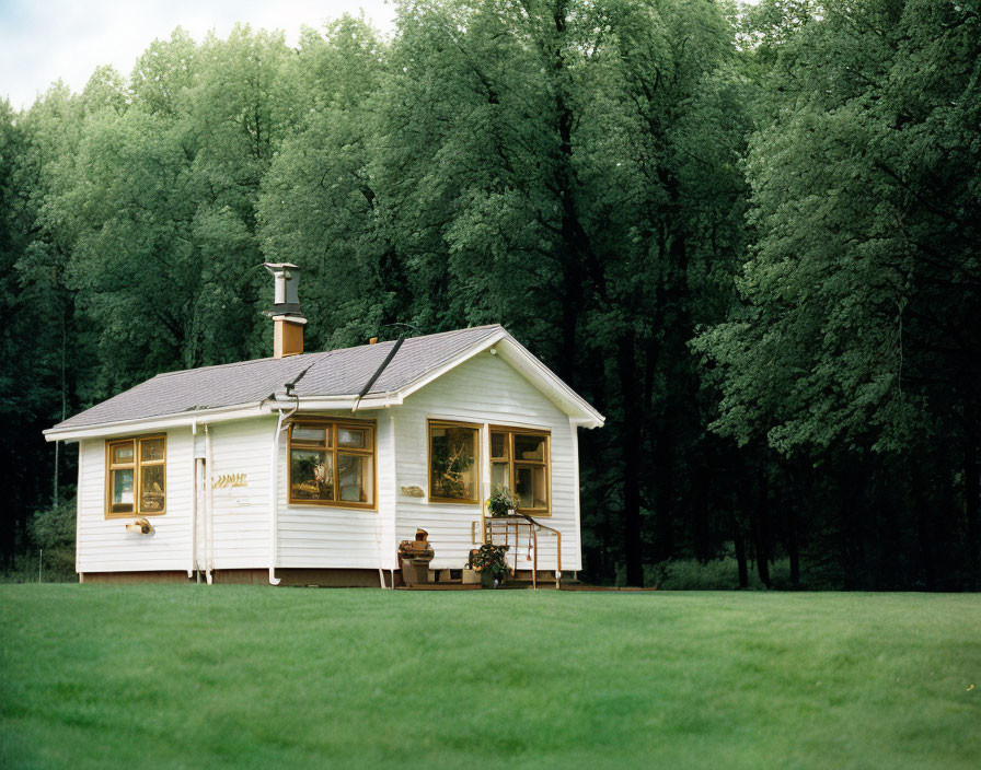 White Cottage with Chimney in Lush Meadow Surrounded by Green Trees