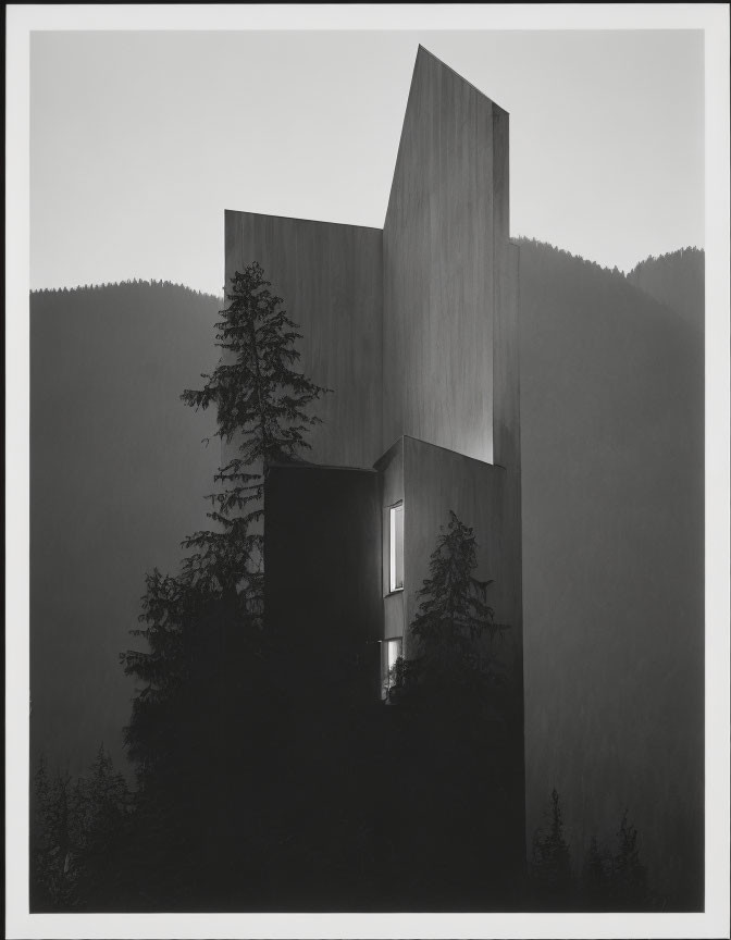 Monochrome photo: Modern building in forested hills with glowing window