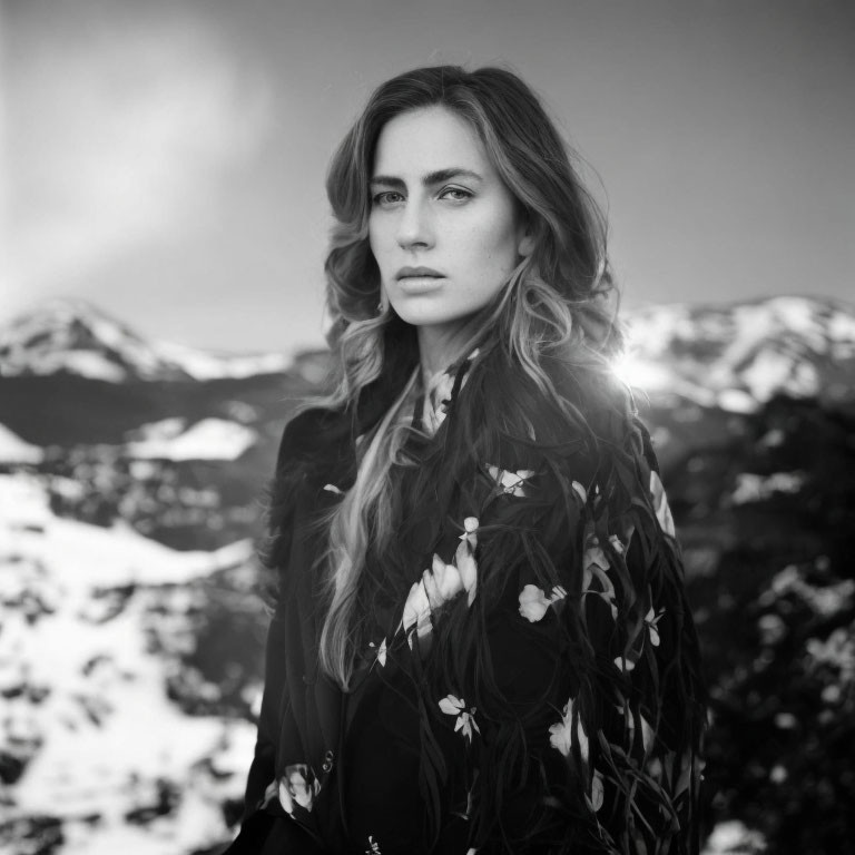 Monochrome portrait of woman with long hair in floral dress against snowy mountains