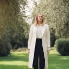 Professional individual in white jacket and black pants against blurred green background.