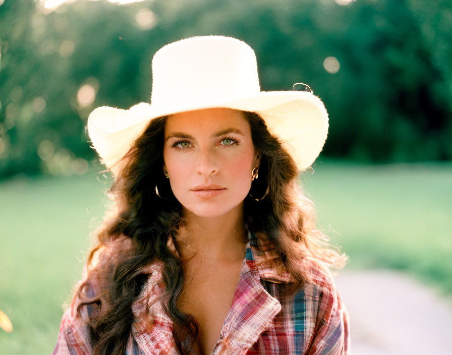 Long-haired woman in wide-brimmed hat and plaid shirt outdoors.