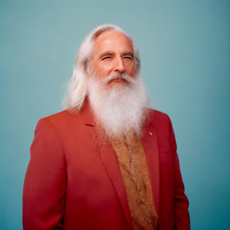 Elderly man with long white beard smiling in red suit on blue background