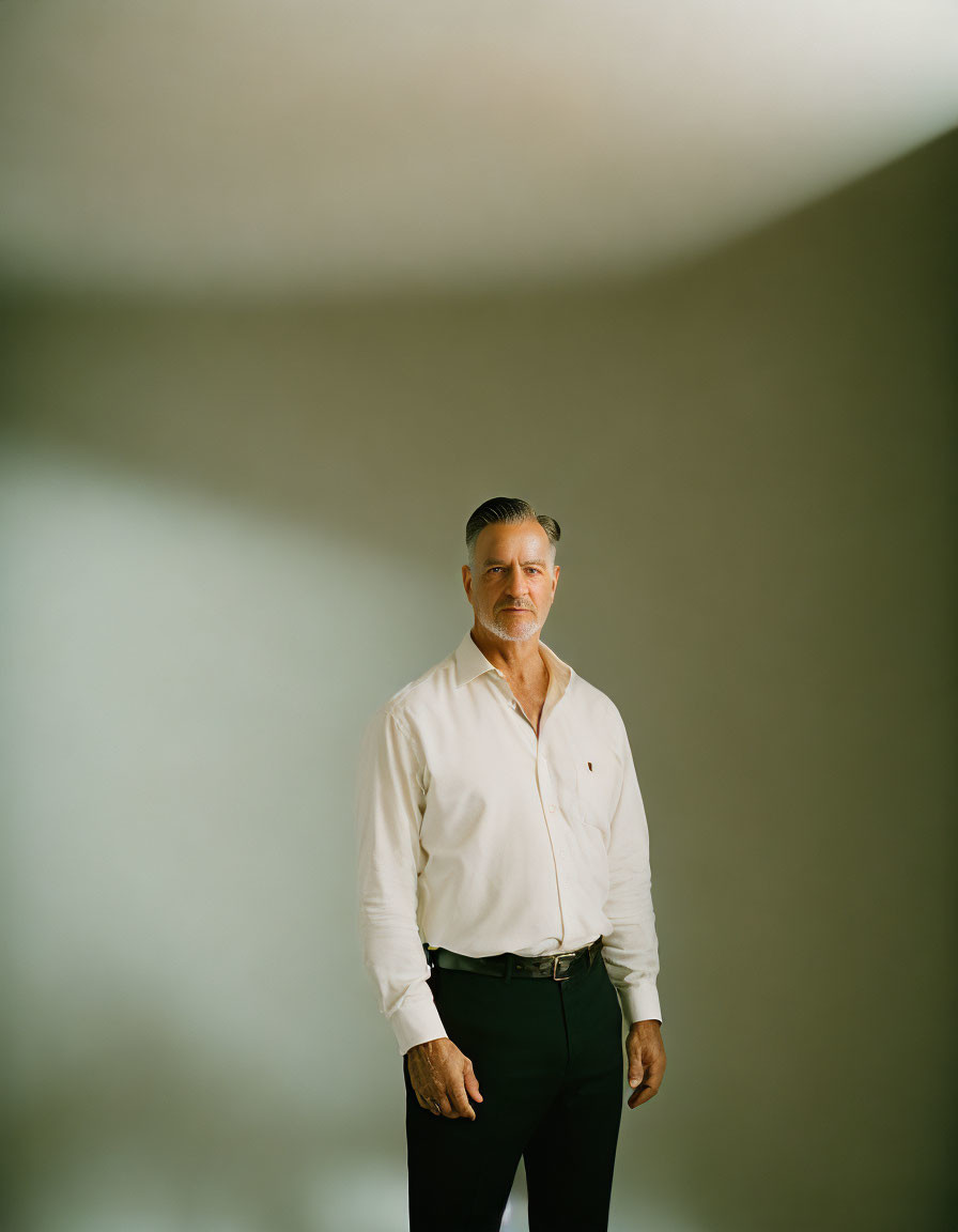 Confident man in white shirt and dark pants against neutral backdrop