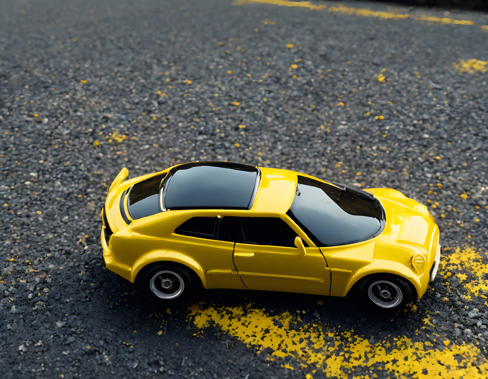 Yellow Toy Car with Black Tinted Windows on Asphalt with Yellow Paint Specks