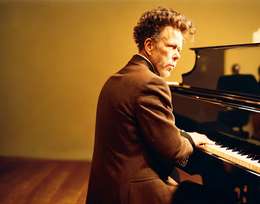 Intense man playing grand piano in warmly lit room