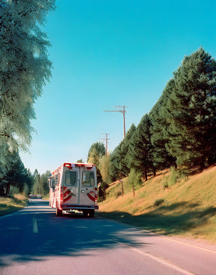 Ambulance parked on road with green trees under clear blue sky