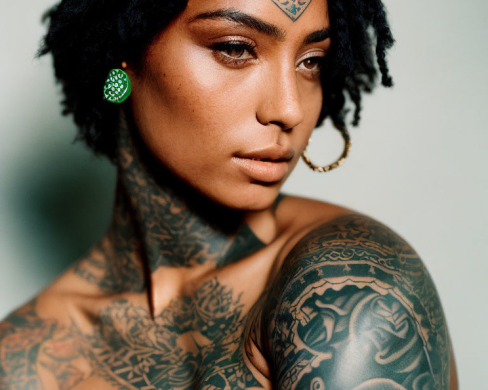 Portrait of woman with intricate tattoos, green earring, and nose ring