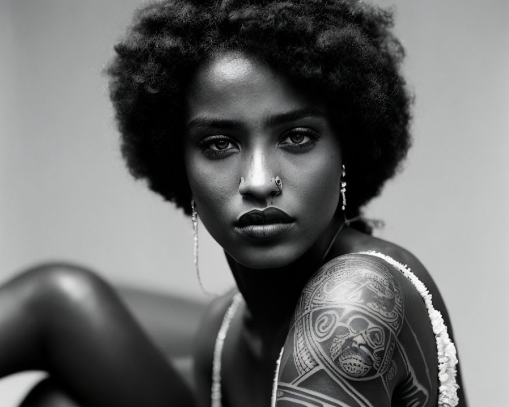 Black and white portrait of woman with afro hair, nose piercing, and tattooed arm in lace