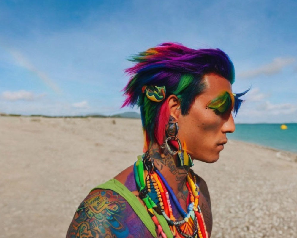 Rainbow-haired person with vibrant makeup on beach with tattoos and colorful accessories