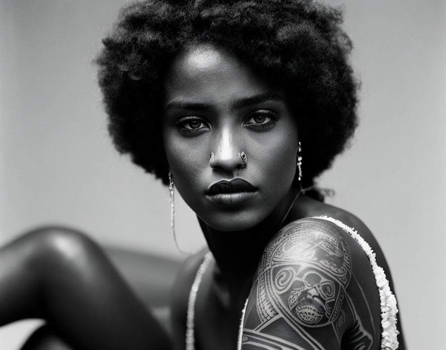 Black and white portrait of woman with afro hair, nose piercing, and tattooed arm in lace