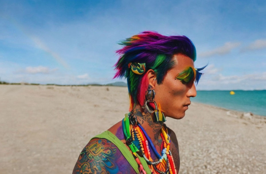 Rainbow-haired person with vibrant makeup on beach with tattoos and colorful accessories