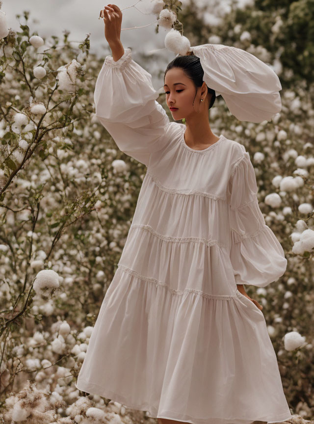 Woman in flowing white dress among fluffy white blooms with oversized sleeves