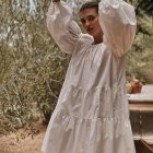 Woman in flowing white dress among fluffy white blooms with oversized sleeves