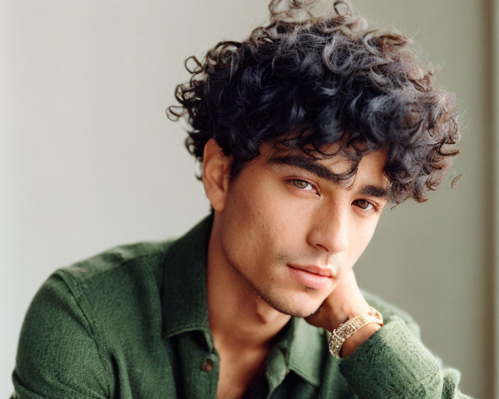 Young man with curly hair in green shirt gazing thoughtfully.