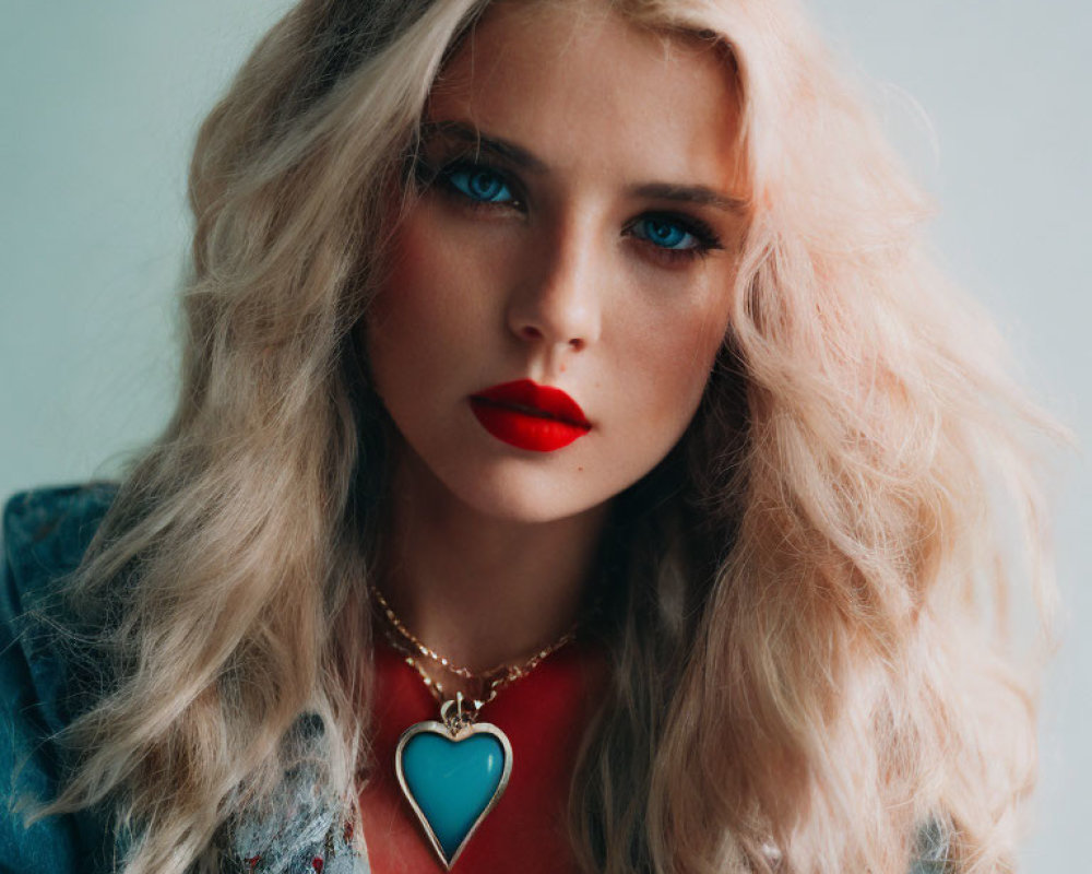 Portrait of woman with wavy blonde hair, blue eyes, red lipstick, denim jacket, heart pendant