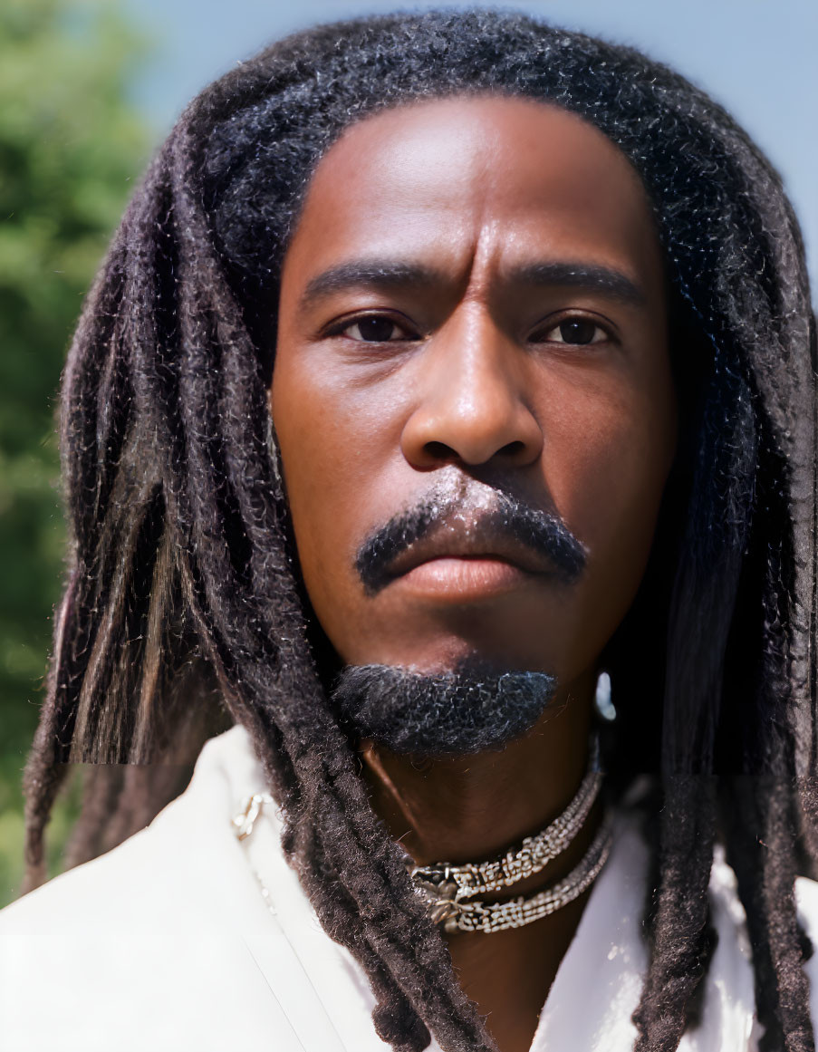 Serious man with dreadlocks and beard in white shirt on green background