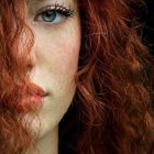 Woman with Flowing Red Hair and Striking Blue Eyes on Dark Background