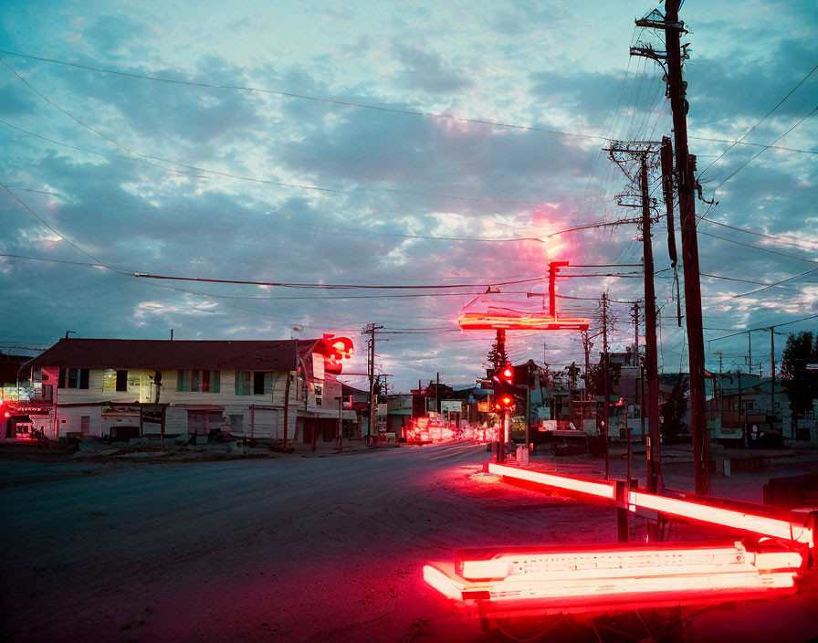 Neon-lit street at dusk with striking red glow, power lines, and cloud-streaked