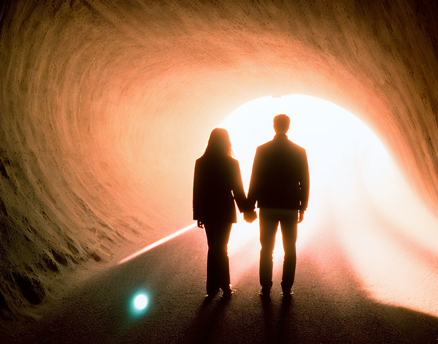 Silhouette of couple holding hands in tunnel with luminous light