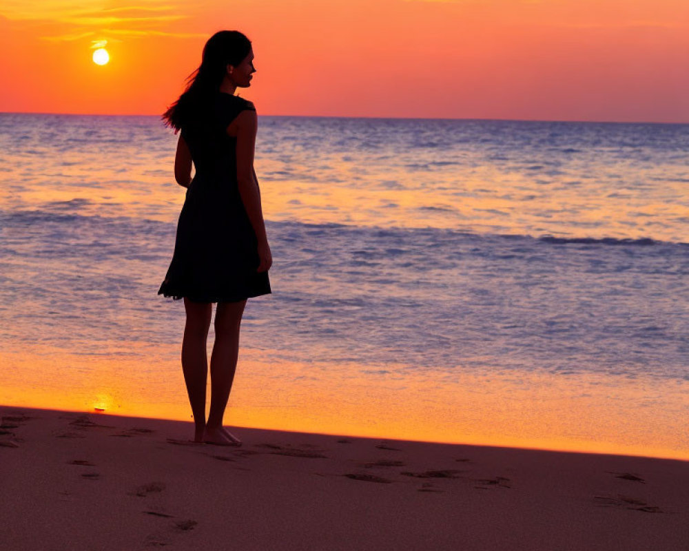 Woman silhouette standing on beach at sunset with low sun and water reflection