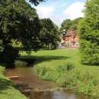 Tranquil landscape painting of lush park with pond and brick building