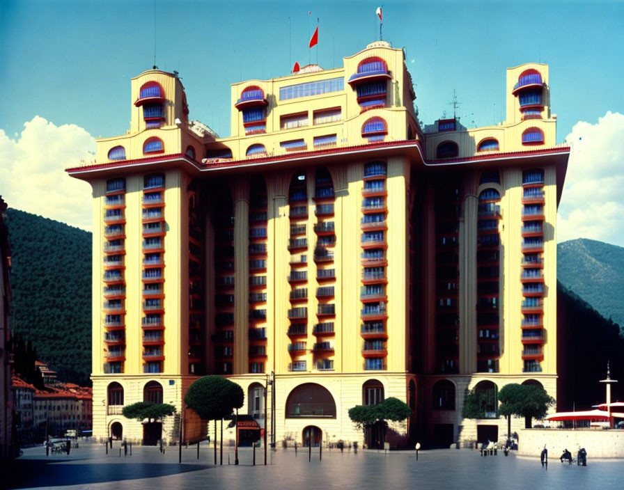 Ornate multi-story building with red tiled roof and decorative balconies against mountain backdrop