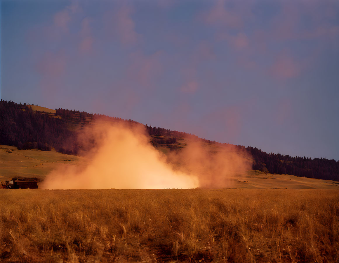 Scenic golden hour lighting on rural landscape with dust cloud and forested hillside