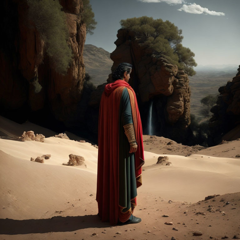 Person in red cape and green tunic on sand dune overlooking rocky canyon with waterfalls