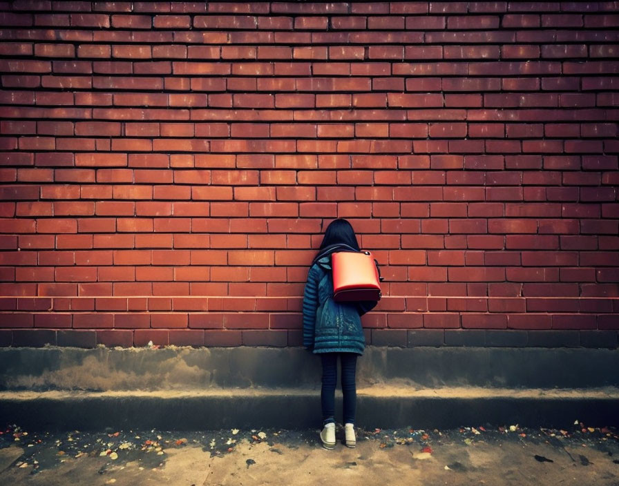 Child with Red Backpack Standing by Red Brick Wall