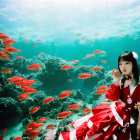 Woman in red dress surrounded by red fish underwater among coral reefs