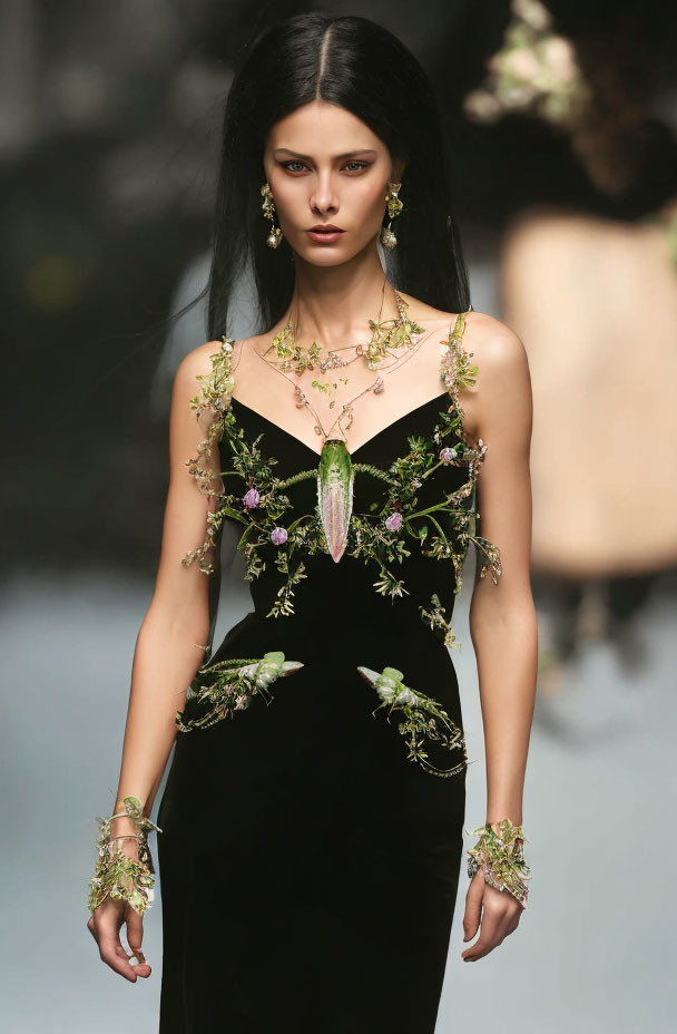 Dark-haired woman in black dress with green and purple floral details on runway