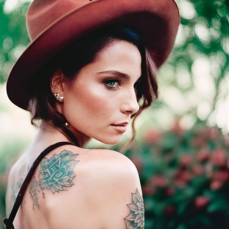 Woman with shoulder tattoo wearing hat, blurred greenery and flowers background