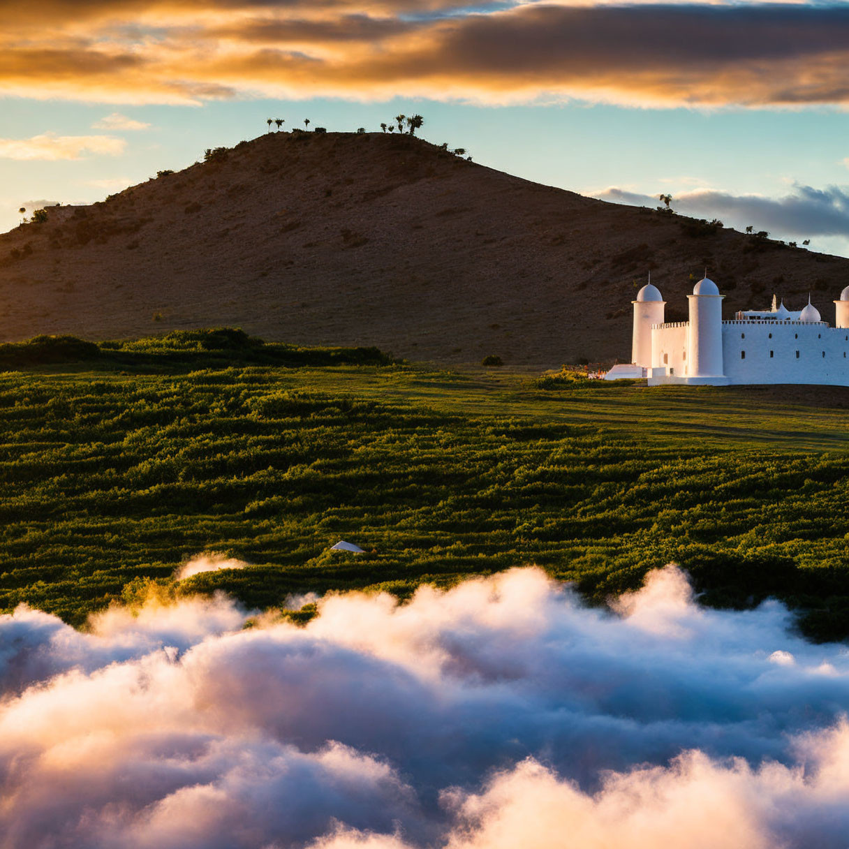 White Building with Cylindrical Towers and Sunset Light Above Clouds