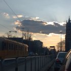 Person walking towards sunset-lit street with vintage trams and ornate buildings