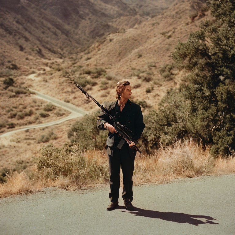 Man standing on road with hilly terrain, holding camera tripod