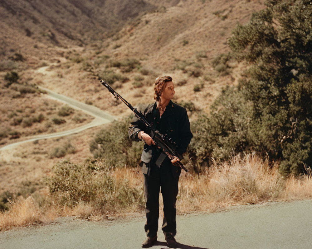 Man standing on road with hilly terrain, holding camera tripod