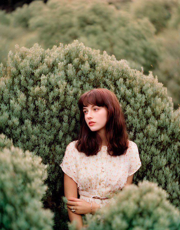 Young woman with brown hair in floral blouse surrounded by green foliage