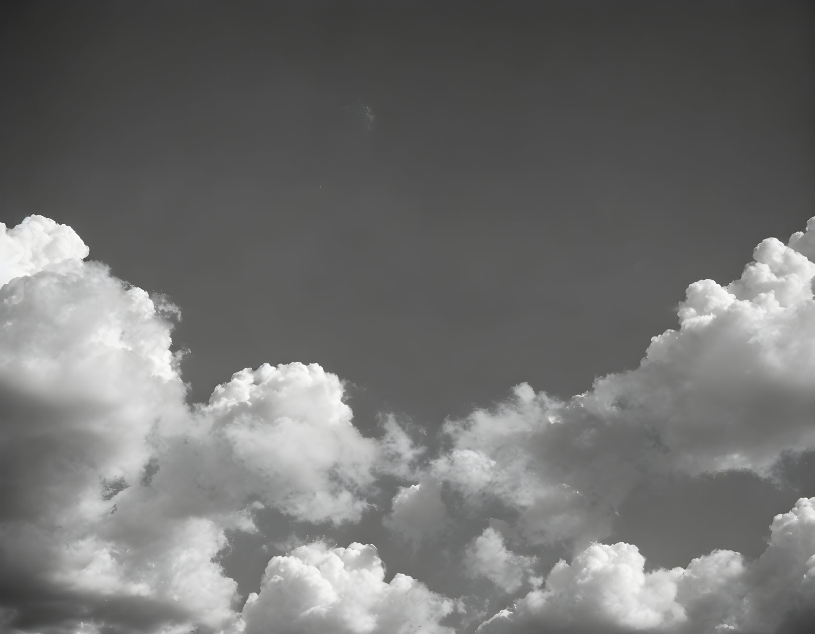 Tranquil grey sky with fluffy white clouds and sunlight peeking through