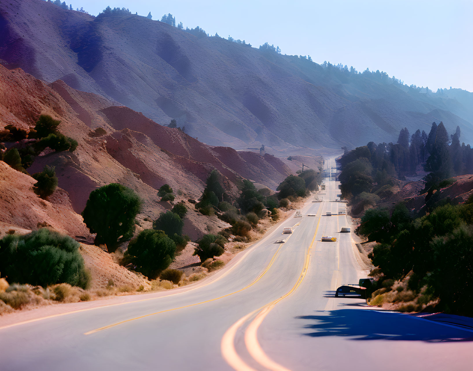 Desert landscape with winding road and vehicles under clear sky