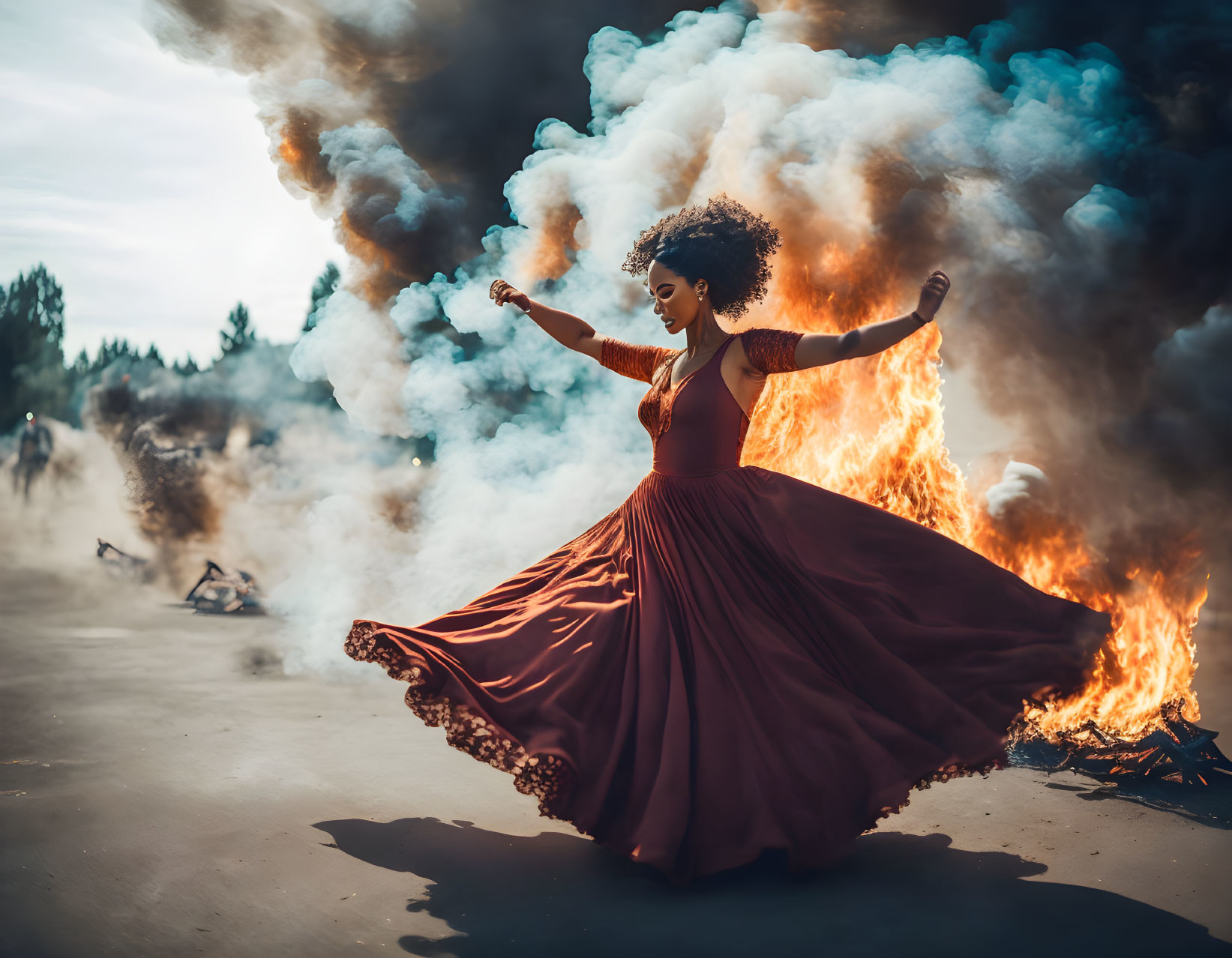 Woman in flowing red dress dances in front of fiery blaze with swirling smoke