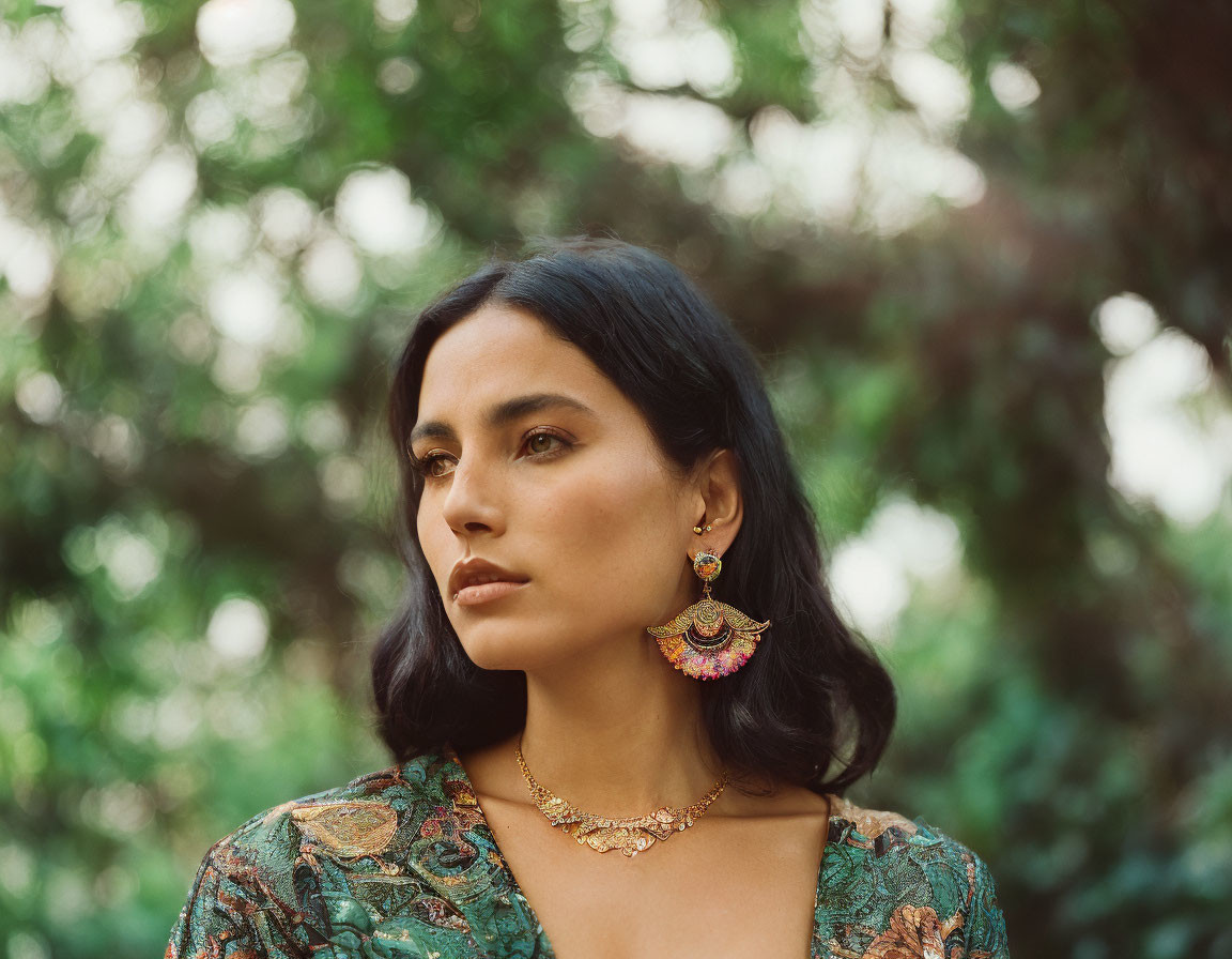 Dark-haired woman in green patterned garment with earrings on blurred green background