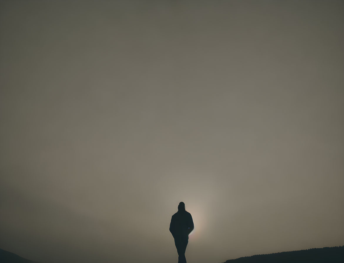 Person's silhouette against low sun horizon in serene sky