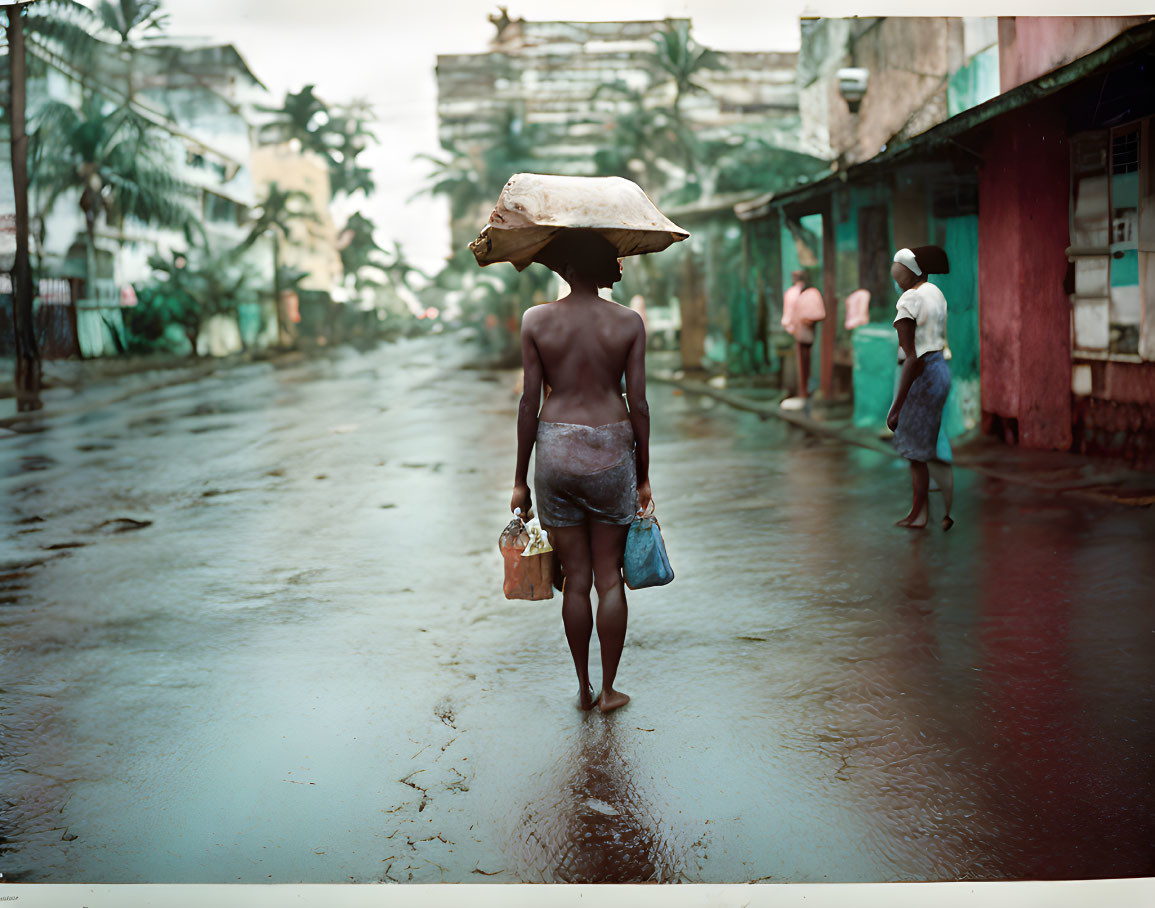 Person walking barefoot with flat object on head in tropical setting